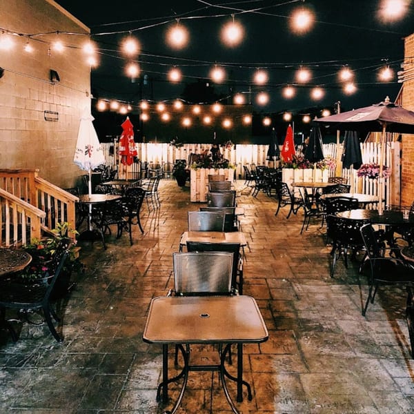 The Harp And Fiddle's outdoor patio at night, illuminated by string lights, with tables and chairs.