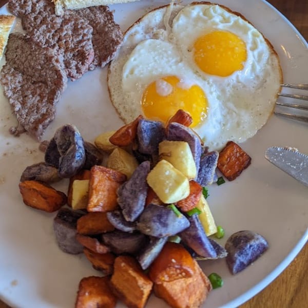 A full Irish breakfast with fried eggs, sausage patties, and colorful roasted potatoes.
