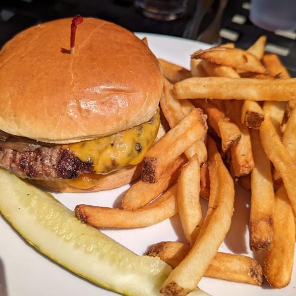 A Harp And Fiddle cheeseburger with fries and a pickle spear on a white plate.