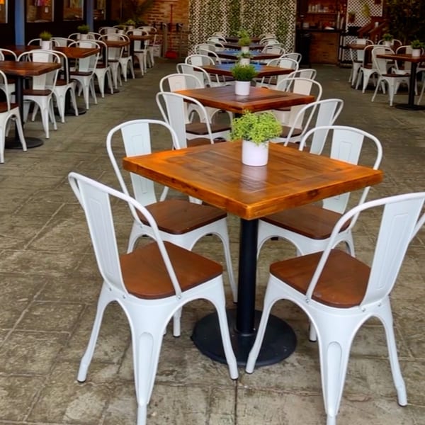 Outdoor dining area at The Harp And Fiddle with white chairs and wooden tables, some with small plants.