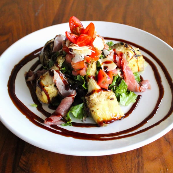 A Harp And Fiddle salad with prosciutto, grilled artichokes, tomatoes, parmesan, and balsamic glaze.