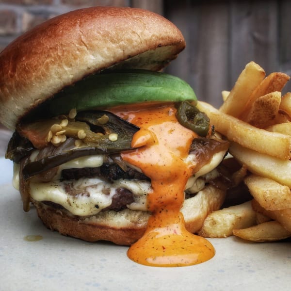 A Harp And Fiddle burger with avocado, peppers, cheese, and sauce, served with fries.