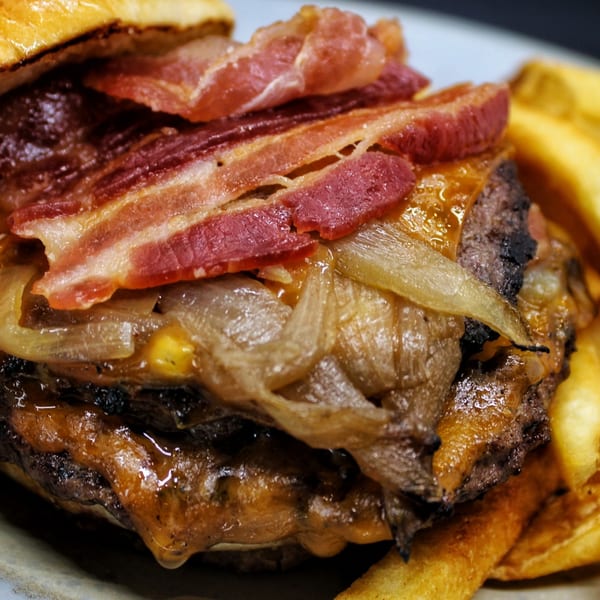 Close-up of a Harp And Fiddle burger with bacon, caramelized onions, and melted cheese, with fries.