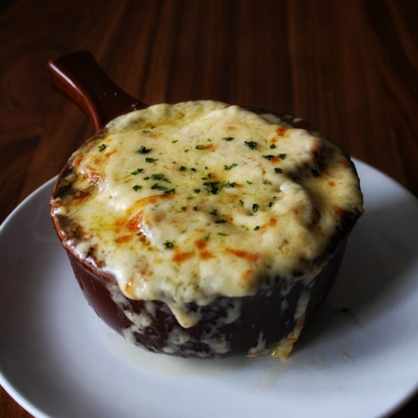 A crock of Irish onion soup with melted, bubbly cheese and herbs on a white plate.