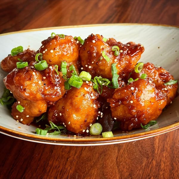 A bowl of Harp And Fiddle's sticky Irish chicken bites, garnished with sesame seeds and green onions.
